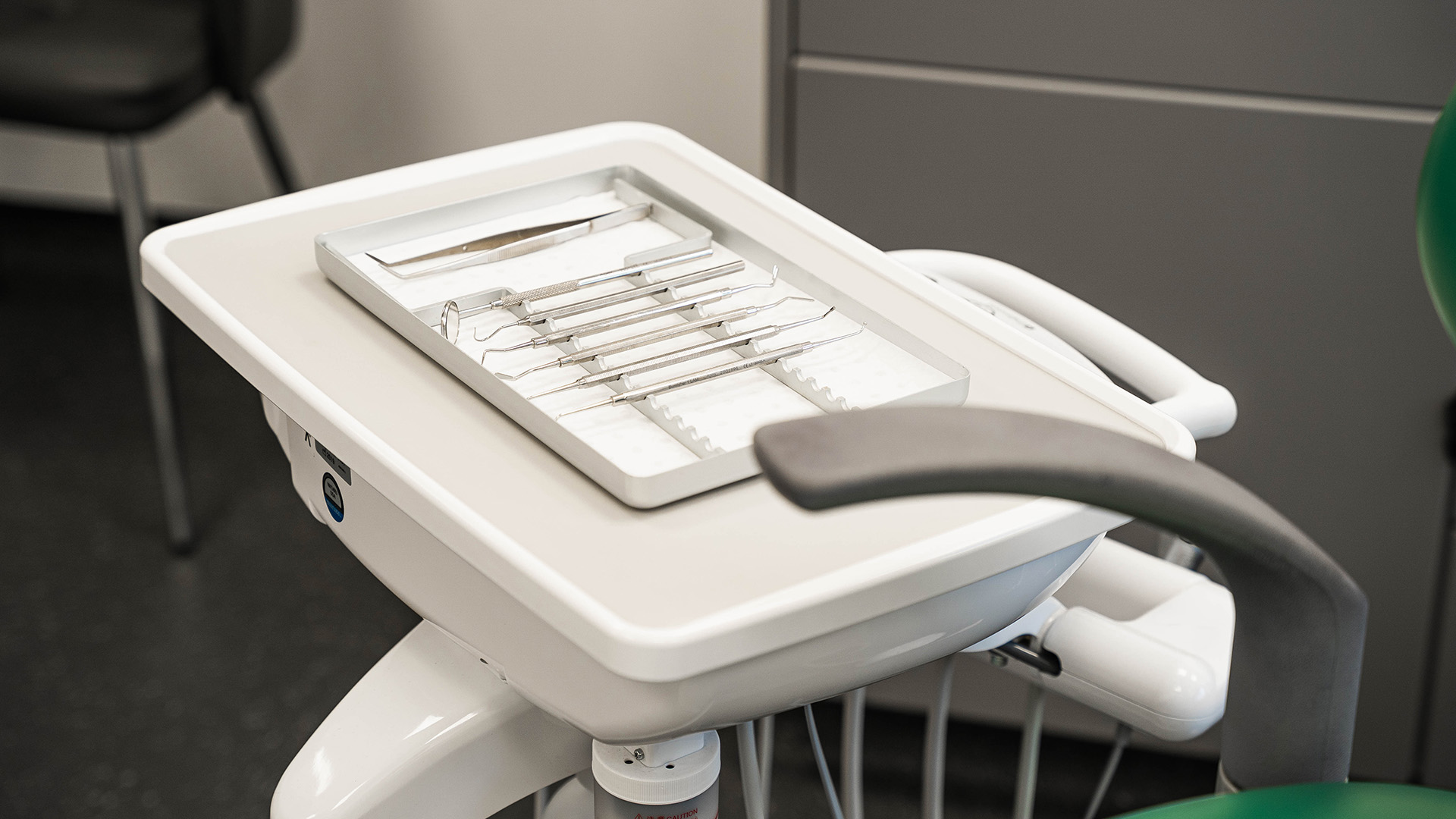 Dentists tools lined up on a tray next to a dentists chair.